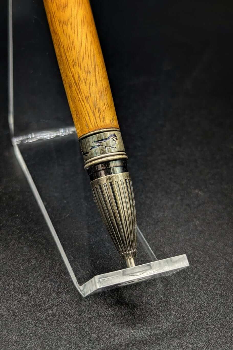 Stylo artisanal fait à la main en bois et résine acrylique colorée, posé sur un support avec fond noir