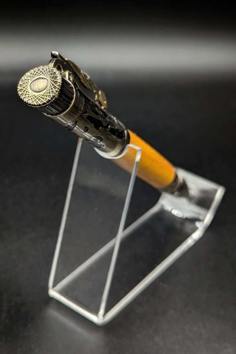 Stylo artisanal fait à la main en bois et résine acrylique colorée, posé sur un support avec fond noir