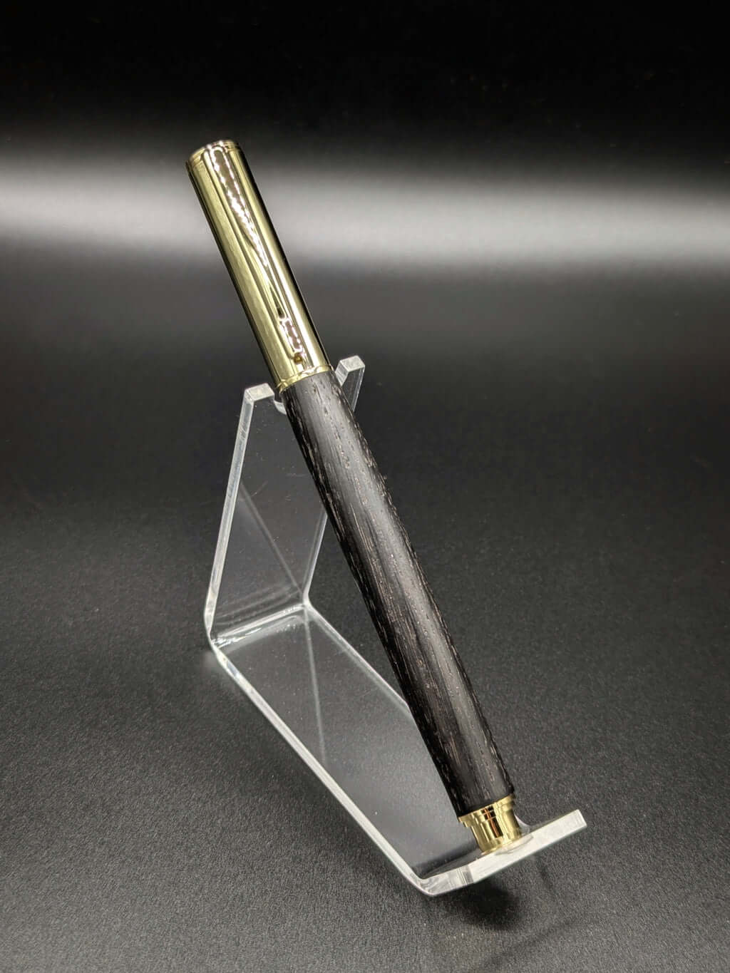 Stylo artisanal fait à la main en bois et résine acrylique colorée, posé sur un support avec fond noir