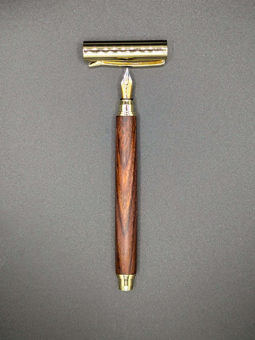 Stylo artisanal fait à la main en bois et résine acrylique colorée, posé sur un support avec fond noir