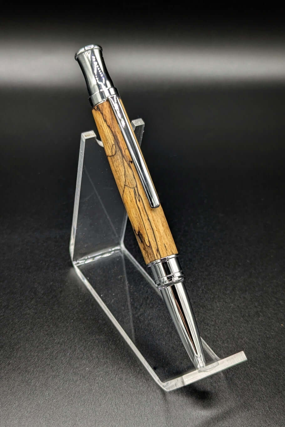 Stylo artisanal fait à la main en bois et résine acrylique colorée, posé sur un support avec fond noir