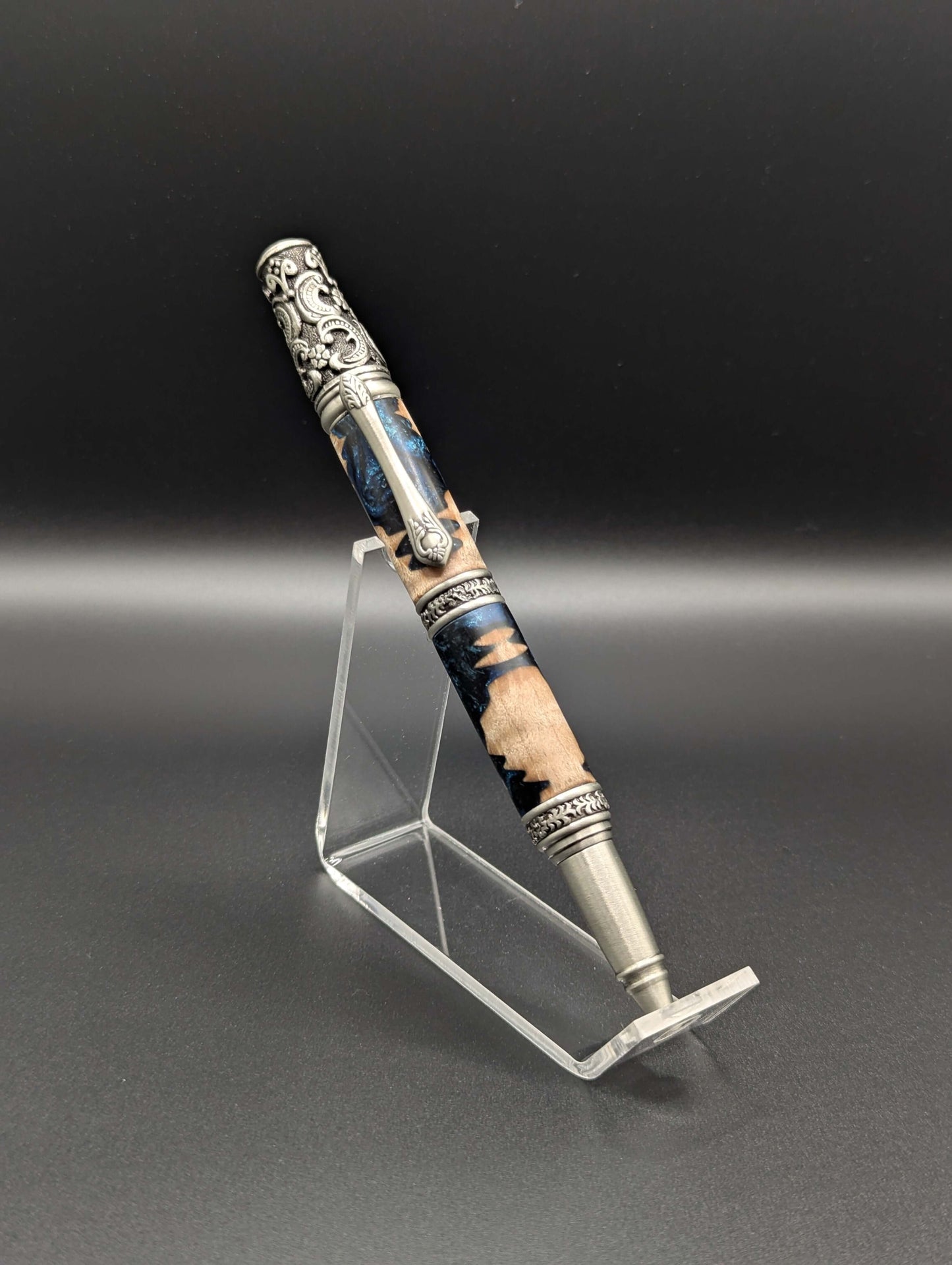 Stylo artisanal fait à la main en bois et résine acrylique colorée, posé sur un support avec fond noir