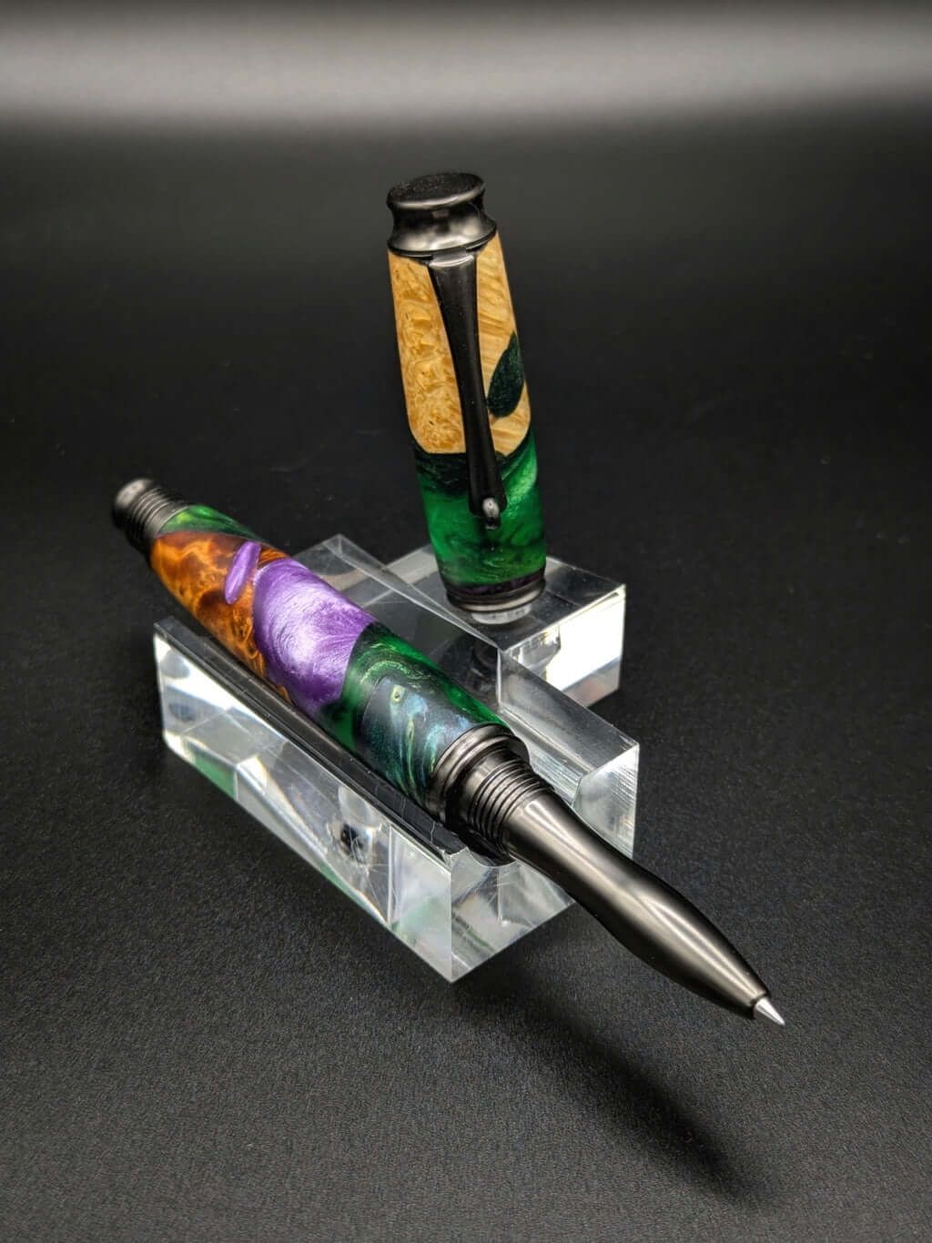 Stylo artisanal fait à la main en bois et résine acrylique colorée, posé sur un support avec fond noir