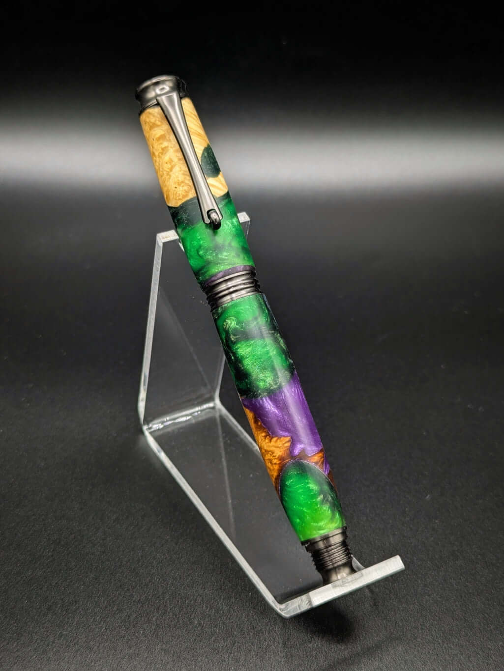 Stylo artisanal fait à la main en bois et résine acrylique colorée, posé sur un support avec fond noir