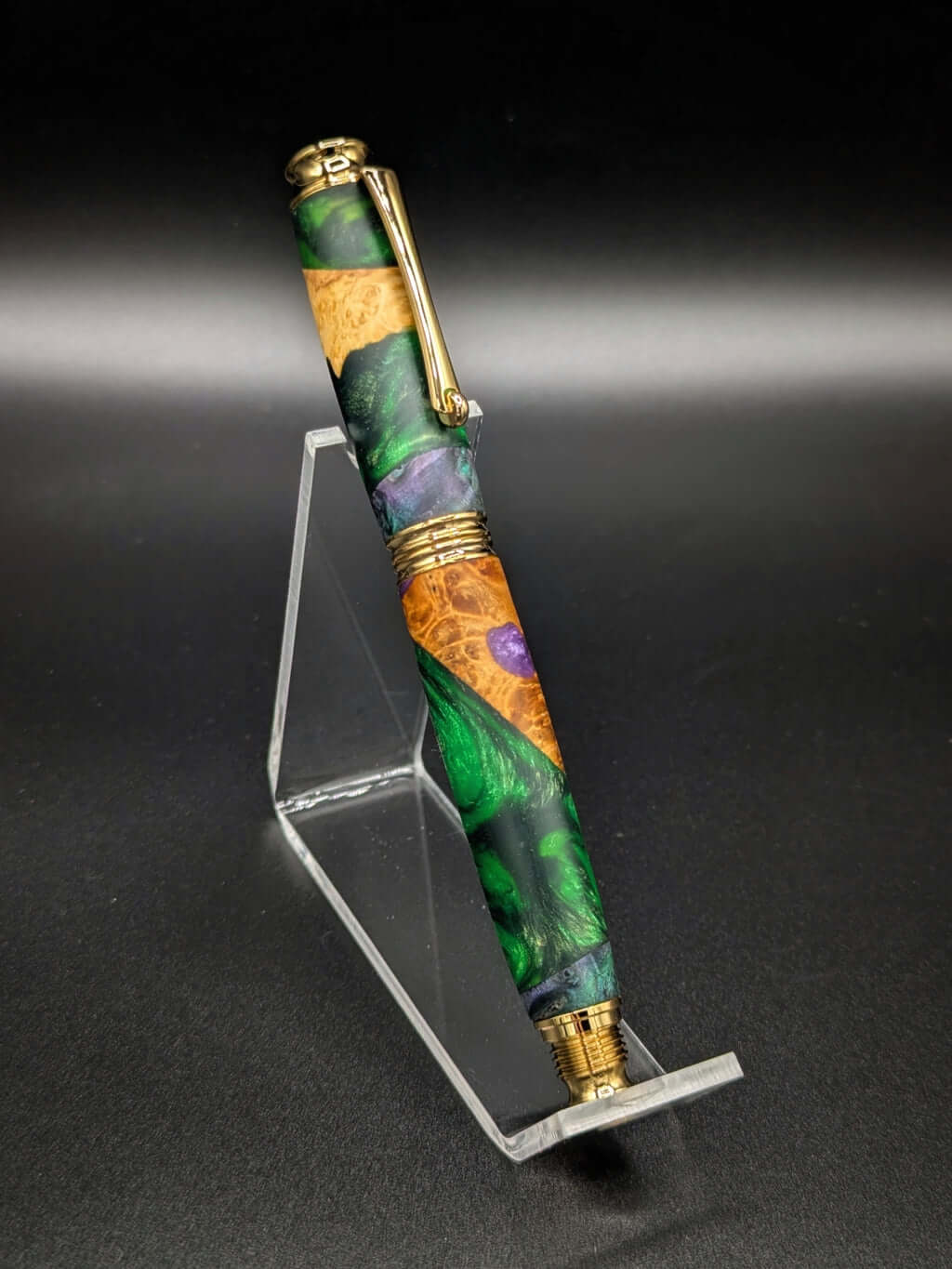 Stylo artisanal fait à la main en bois et résine acrylique colorée, posé sur un support avec fond noir