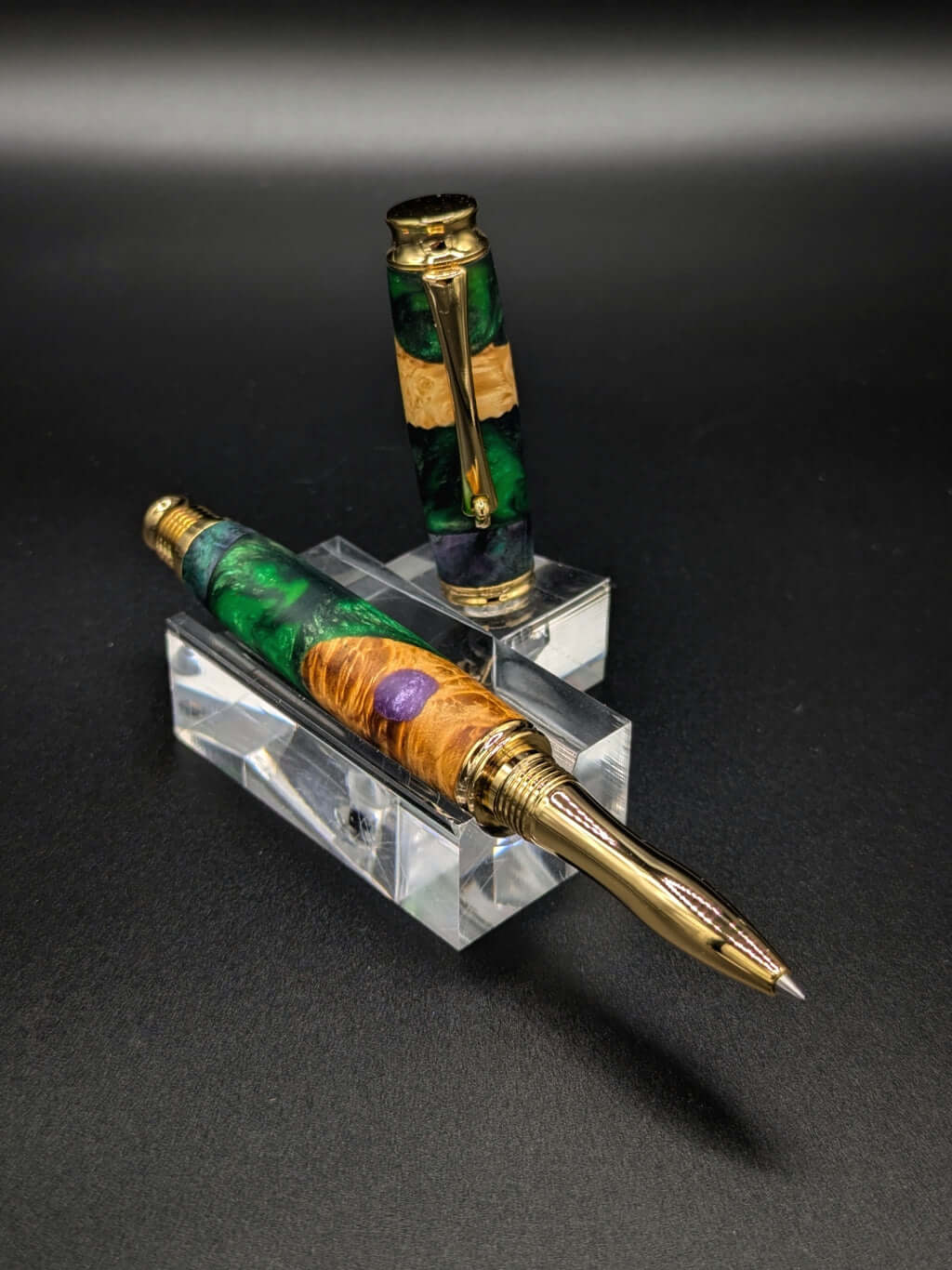 Stylo artisanal fait à la main en bois et résine acrylique colorée, posé sur un support avec fond noir